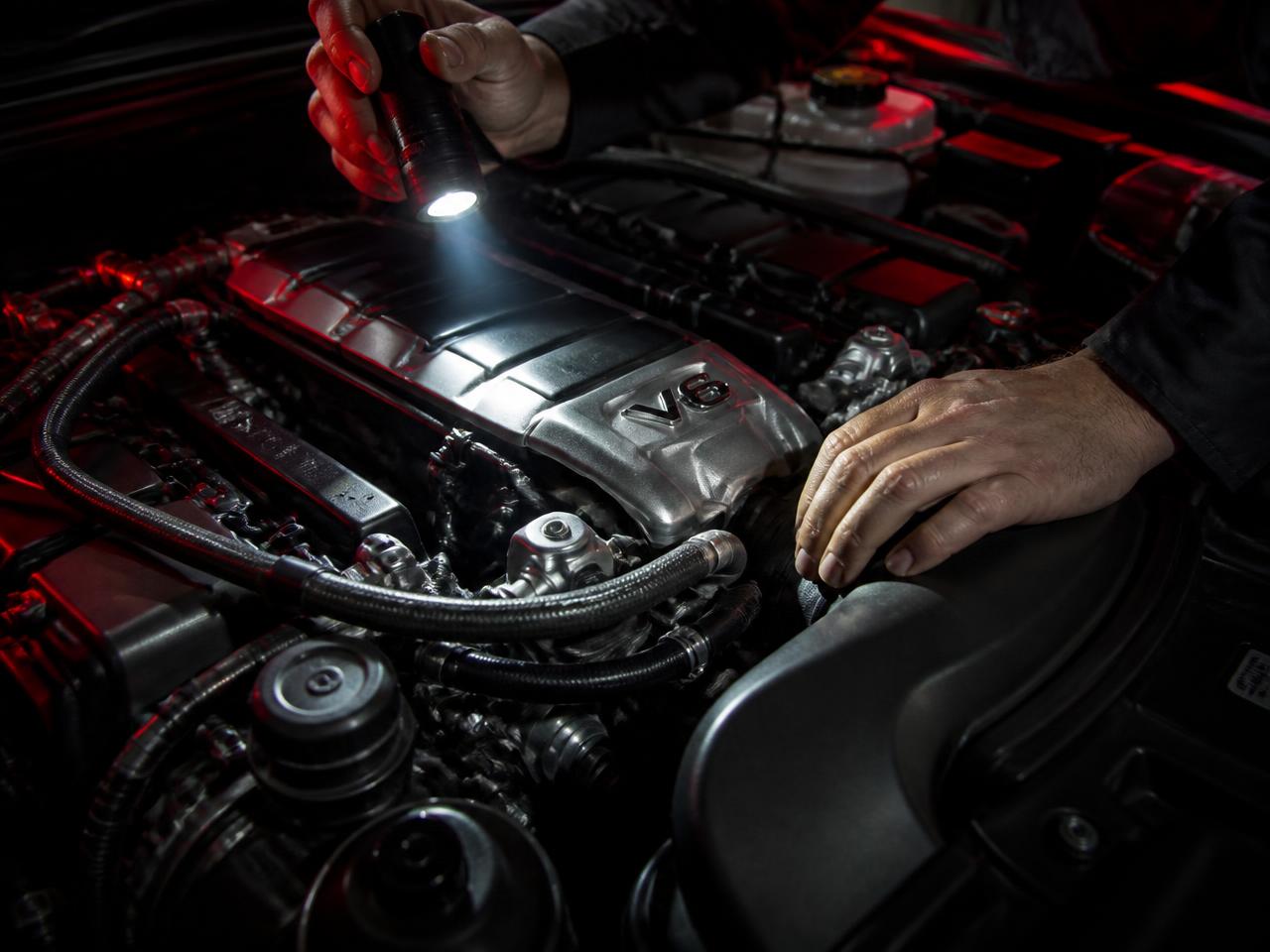 Mechanic inspecting a car engine bay with a torch